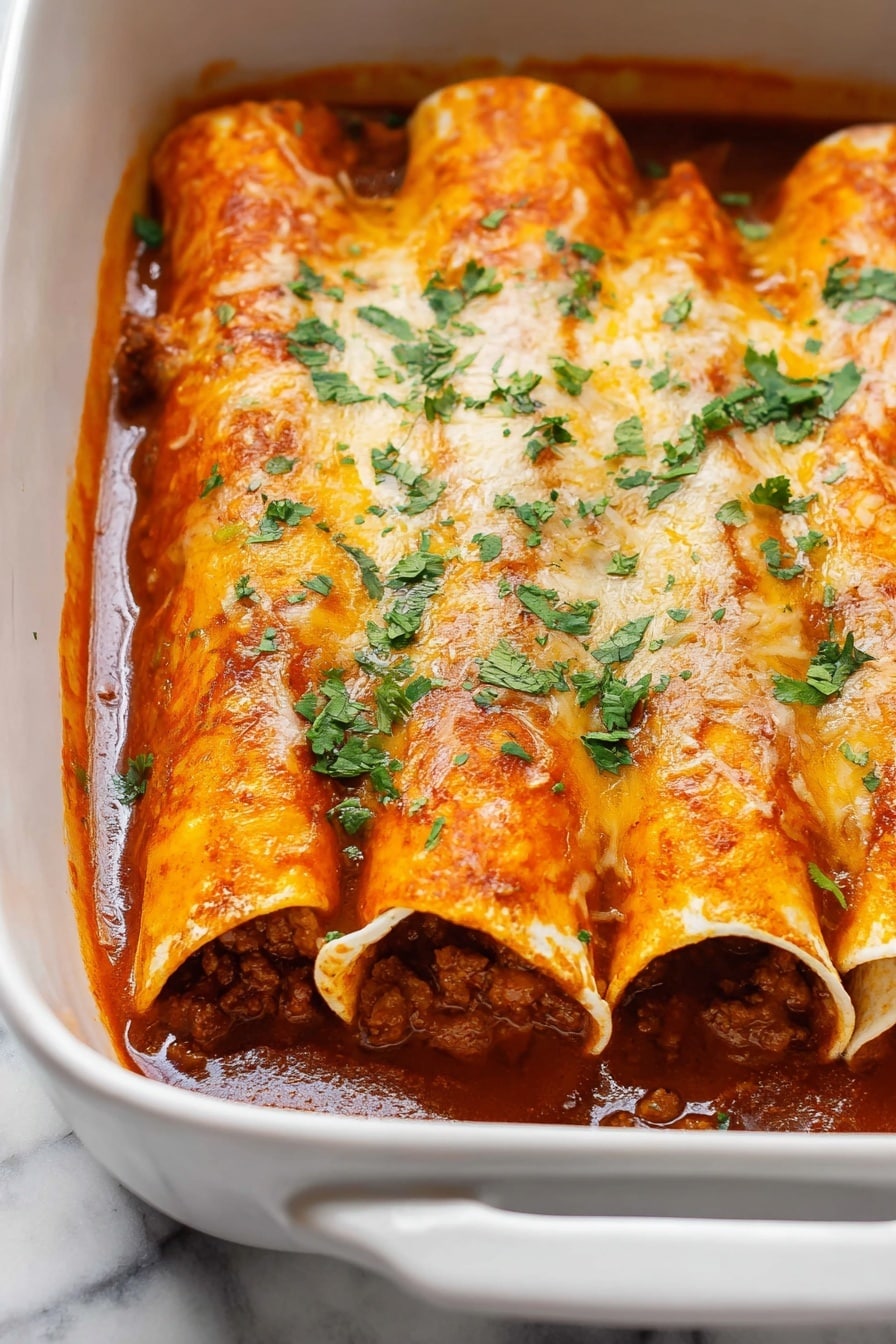 Beef Enchiladas - The image shows a white baking dish filled with four rolled enchiladas placed side by side. Each enchilada is covered with a thick, bright orange-red sauce and melted cheese that is slightly golden and smooth in texture. Inside the enchiladas, you can see a rich, dark brown meat filling that looks moist and chunky. Fresh, chopped green cilantro is sprinkled evenly on top, adding a pop of color. The sauce inside the dish pools slightly around the bottom edges, giving a saucy and inviting look. The dish is sitting on a white marbled surface. Photo taken with an iphone --ar 2:3 --v 7