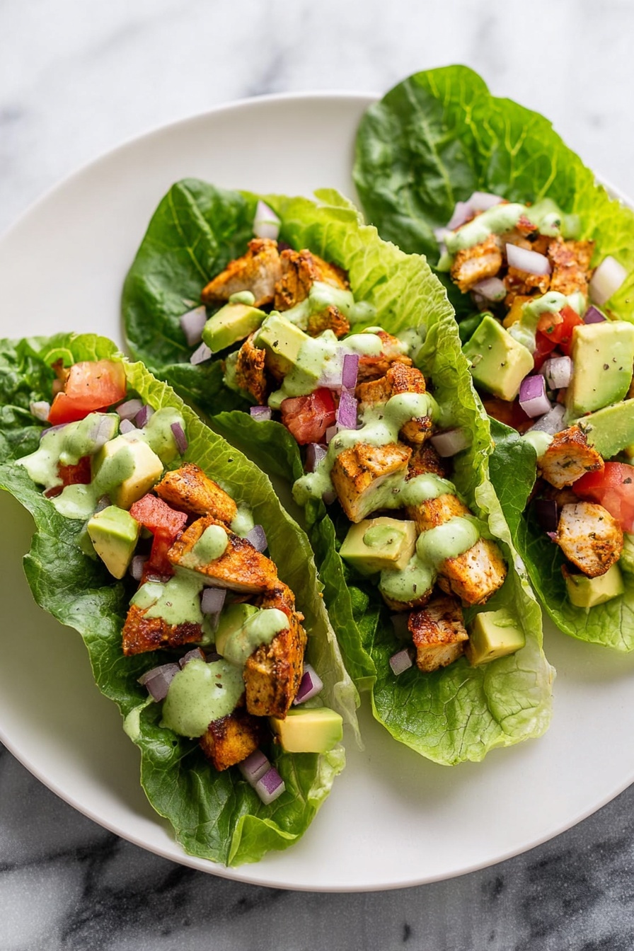 The image shows three lettuce wraps placed side by side on a large white plate set on a white marbled surface. Each wrap is made with one long dark green leaf of lettuce as the base layer. On top of the lettuce, there are chunks of cooked golden brown chicken, followed by diced avocado pieces and small bits of red tomato and purple onion scattered evenly. A creamy green sauce is drizzled over all the wraps, blending smoothly with the other ingredients. The overall look is fresh and colorful. Photo taken with an iphone --ar 2:3 --v 7