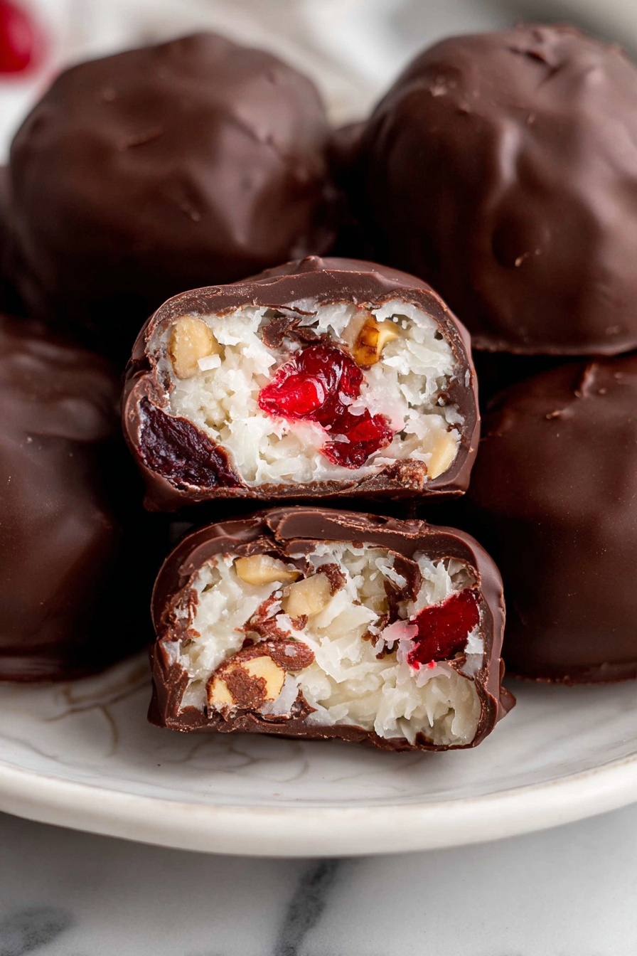 The image shows several round chocolate-covered candies on a white plate with a subtle design. One candy is cut in half in the center, revealing three layers inside: a creamy white coconut layer with a soft texture on the outside, bright red cherry pieces mixed in the middle, and small nut pieces embedded throughout. The shiny dark brown chocolate shells are thick and smooth with a few small cracks. The background and surface are white marble. photo taken with an iphone --ar 2:3 --v 7