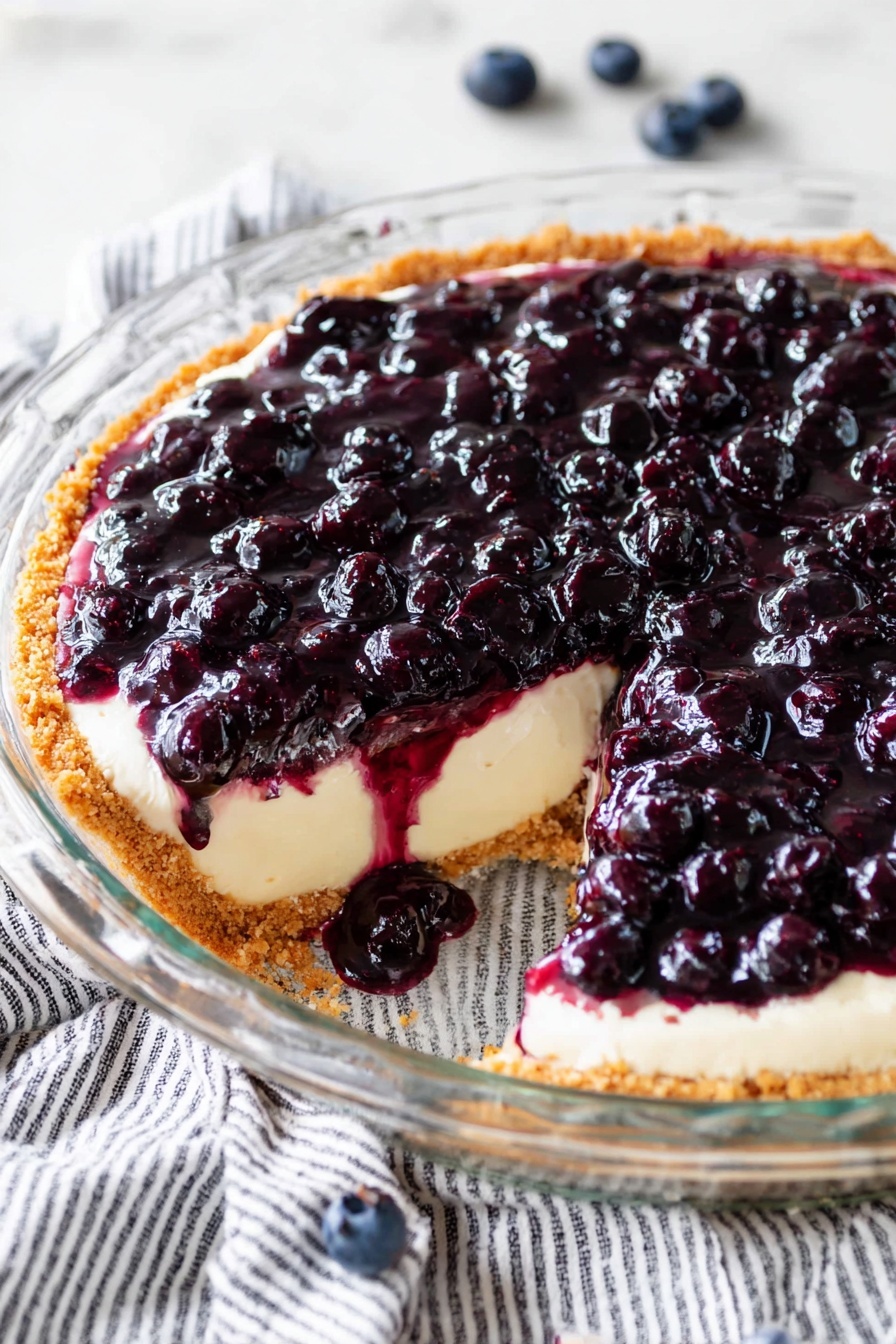 The image shows a clear glass pie dish on a white marbled surface with a striped cloth underneath. The pie has three visible layers: the bottom layer is a light beige crust with a crumbly texture, the middle layer is a smooth cream filling, and the top layer is a thick, glossy topping full of dark purple and black blueberries covered in syrup. A large slice is missing, revealing the cream layer and some of the syrup dripping on the white marbled surface. There are a few loose blueberries scattered around the dish. photo taken with an iphone --ar 2:3 --v 7