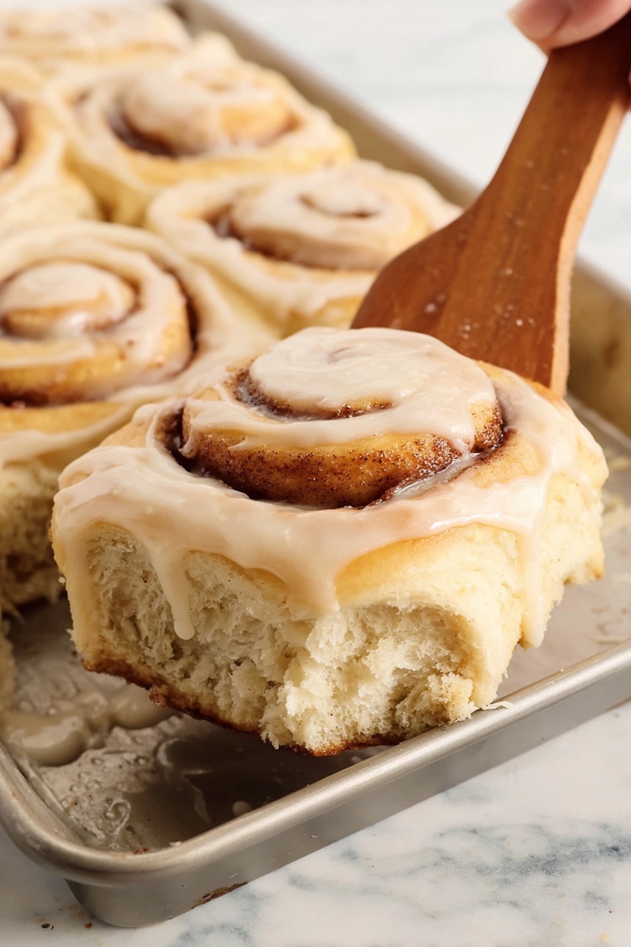 A white plate holds a cinnamon roll with a visible bite taken out of it, showing its soft, fluffy layers inside and a swirl of brown cinnamon filling. The roll is topped with a light cream-colored icing that drips slightly onto the plate. The plate sits on a textured blue cloth on a white marbled surface. In the background, there is a white pitcher with a thin dark rim and a gold fork resting nearby. Also, blurred white flowers and cinnamon sticks add to the warm and cozy feel of the image. Photo taken with an iphone --ar 2:3 --v 7