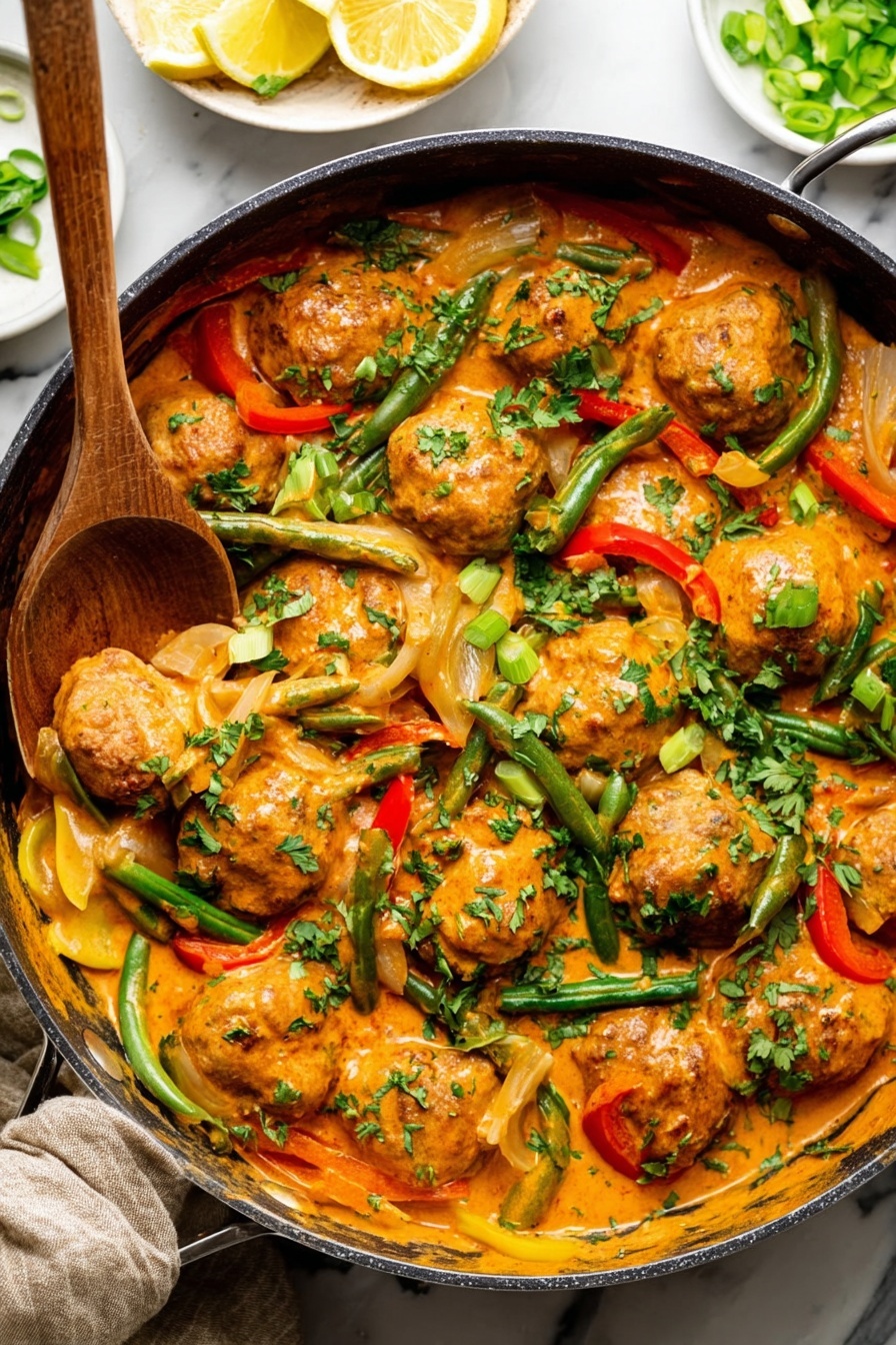 A large pan filled with round meatballs covered in a thick, creamy orange sauce, mixed with green beans, red and yellow bell pepper strips, and sliced onions. The dish is topped with chopped green onions and fresh parsley, adding green color details. A wooden spoon rests inside the pan on the left side, scooping some meatballs and sauce. The background shows a small white bowl with lemon wedges and another with sliced green onions on a white marbled surface. photo taken with an iphone --ar 2:3 --v 7
