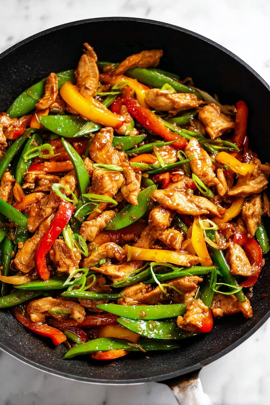 The image shows a black pan filled with stir-fried dish made of many thin pieces of light brown cooked chicken, bright green snap peas, and strips of red and yellow bell peppers. The chicken pieces are mixed evenly with the vegetables, all coated in a glossy brown sauce. The snap peas are shiny and fresh looking, some cut diagonally, and the bell pepper strips add a pop of color around the pan. Small slices of green onion are scattered on top, adding a fresh green touch. The pan rests on a white marbled surface, making the colors of the food stand out clearly. photo taken with an iphone --ar 2:3 --v 7