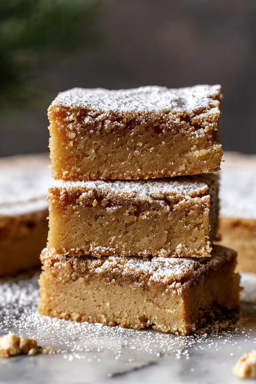 Three square pieces of light brown cake are stacked on top of each other. Each cake piece has a soft, crumbly texture and is dusted with a thin layer of white powdered sugar on top. The edges of the cakes look slightly rough, showing the moist inside. The background has a soft dark blur, and the cakes sit on a white marbled surface with some powdered sugar scattered around. Photo taken with an iphone --ar 2:3 --v 7