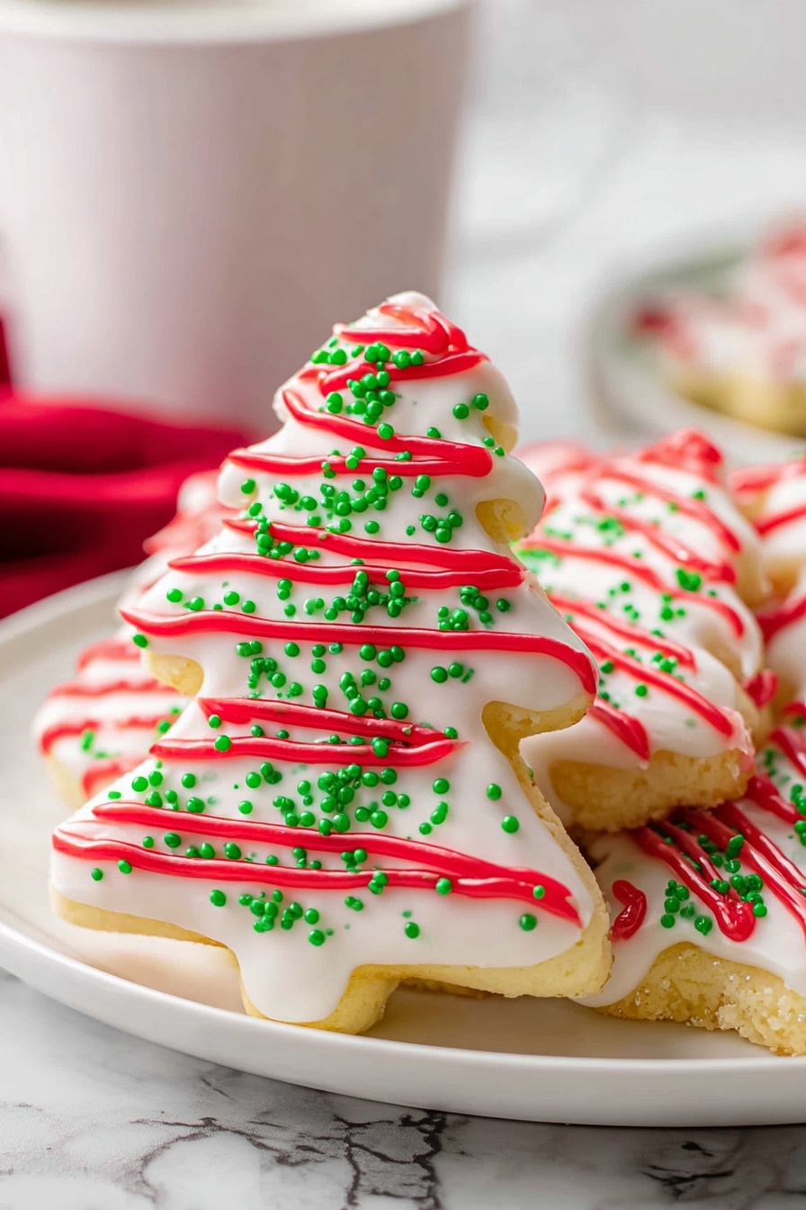 The image shows three triangular cookies stacked on one another on a white plate, each cookie is covered in white icing with green sugar sprinkles scattered all over. Red icing in wavy lines runs across the surface of each cookie, creating a festive contrast. The cookies have a slightly rough texture visible under the icing. The background is a white marbled texture, and there is a blurry white cup behind the plate. photo taken with an iphone --ar 2:3 --v 7