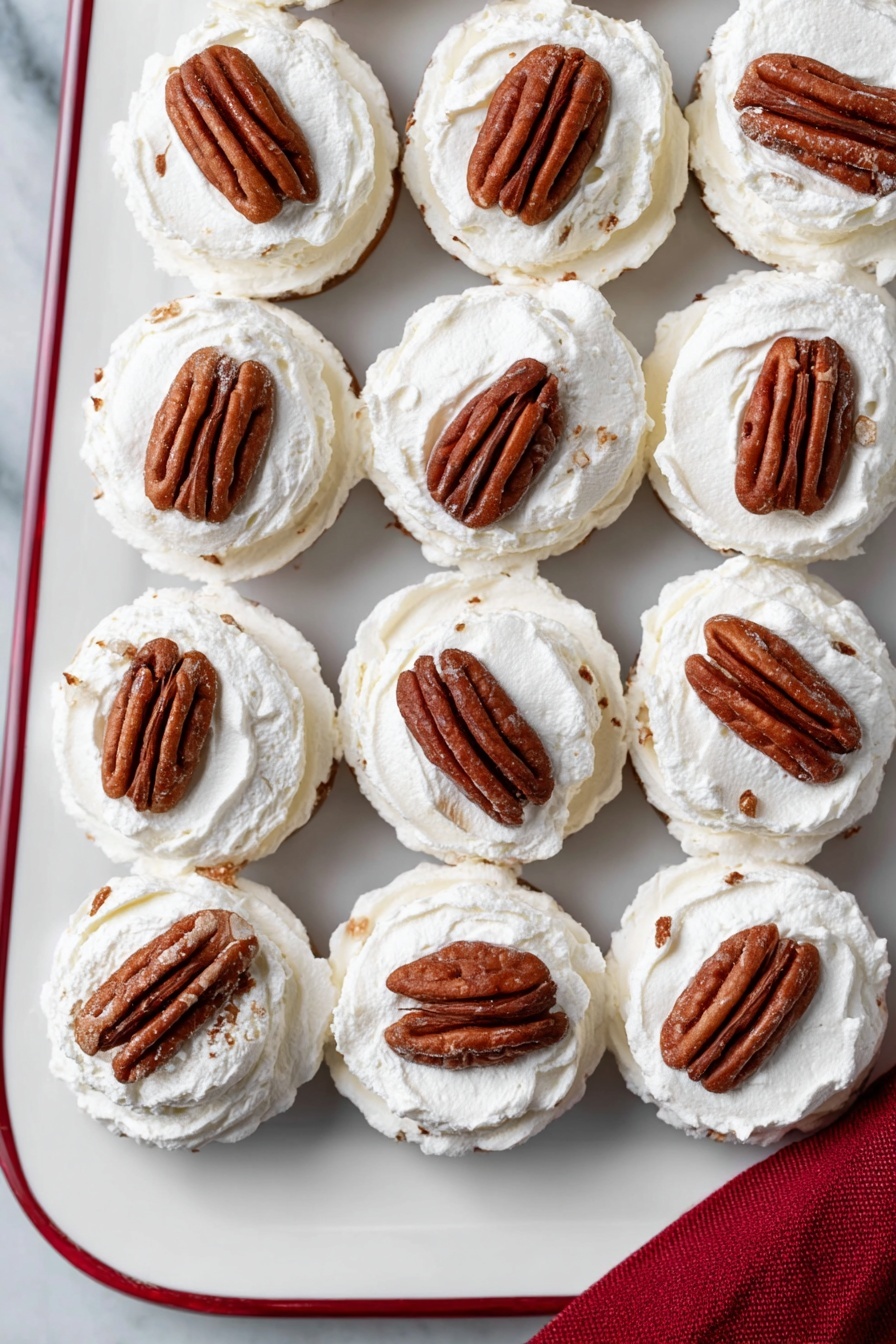 A white tray on a white marbled surface is filled with small dessert rounds arranged in a neat grid, each dessert has two main layers: a soft, white whipped cream layer topped with a whole pecan half, which is brown and textured, slightly pressed into the cream. The whipped cream is fluffy with a slightly uneven texture, and the pecan sits right in the center of each round, creating a contrast between the smooth white cream and the rich brown nut. The tray edge has a thin red line visible, and a corner of a red cloth napkin is seen at the bottom right corner. photo taken with an iphone --ar 2:3 --v 7