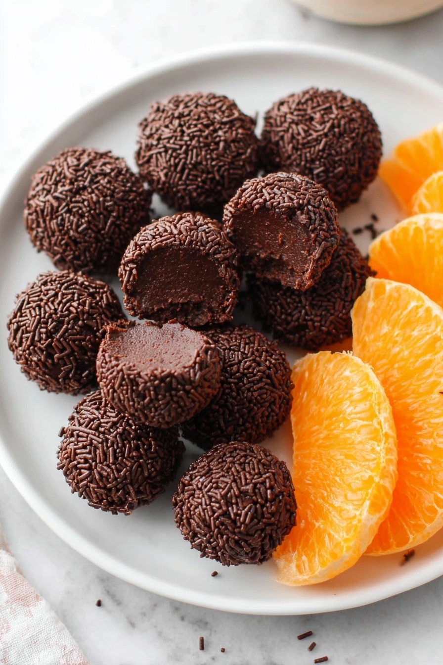 A white plate filled with multiple small round chocolate balls covered in dark chocolate sprinkles, one ball is bitten showing a smooth, dark chocolate inside. On the right side of the plate, there are bright orange slices with a juicy texture. The plate is placed on a white marbled surface. Photo taken with an iphone --ar 2:3 --v 7