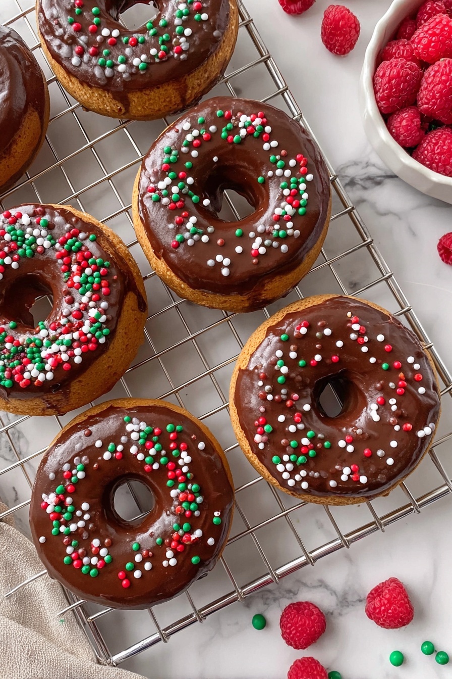 There are five donuts placed on a silver metal cooling rack with a white marbled surface underneath. Each donut has a golden-brown base layer, topped with a smooth, thick layer of shiny chocolate glaze that evenly covers the top. The chocolate glaze is decorated with small, round confetti sprinkles in red, green, and white, scattered randomly over each donut. To the top right, a white bowl holds fresh red raspberries, adding a vibrant color contrast. Additional sprinkles are scattered around the rack and bowl, enhancing the festive look. photo taken with an iphone --ar 2:3 --v 7