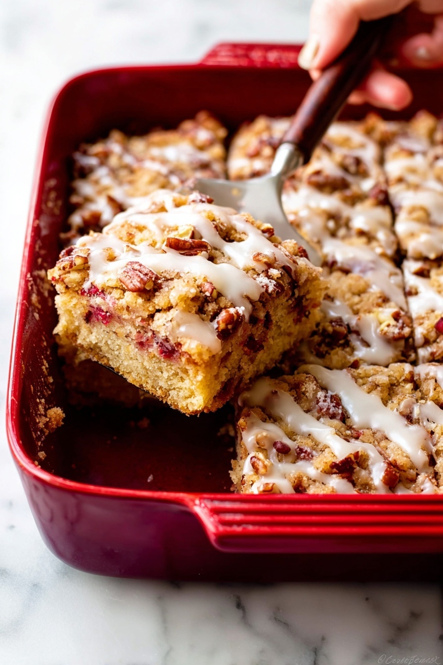 The image shows a red baking dish on a white marbled surface, filled with a dessert that has three clear layers. The bottom layer is light golden cake with bits of dark red fruit inside. The middle layer is crumbly and brown, with a rough texture and a mix of smaller and larger pecan pieces scattered throughout. The top layer is a thin drizzle of white icing that shines slightly over the crumbly nuts and cake below. A woman's hand is holding a spatula lifting a square piece of the dessert from the dish, revealing the soft inside and the mix of fruit and nuts clearly. The edges of the dessert look slightly crunchy, while the inside looks moist and crumbly. photo taken with an iphone --ar 2:3 --v 7