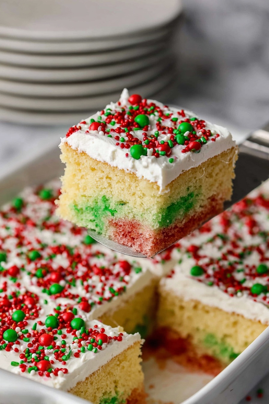 The image shows a square piece of cake being lifted with a silver spatula. The cake has two visible layers of sponge inside, one green on the left and one red on the right, both speckled and moist. On top of these layers, there is a thick layer of white frosting, smooth and creamy, covered with red and green round and small sprinkle decorations, giving a festive look. The cake sits in a white dish with more pieces inside, also topped with the same white frosting and sprinkles. The background is a white marbled surface with stacked white plates slightly out of focus. Photo taken with an iphone --ar 2:3 --v 7