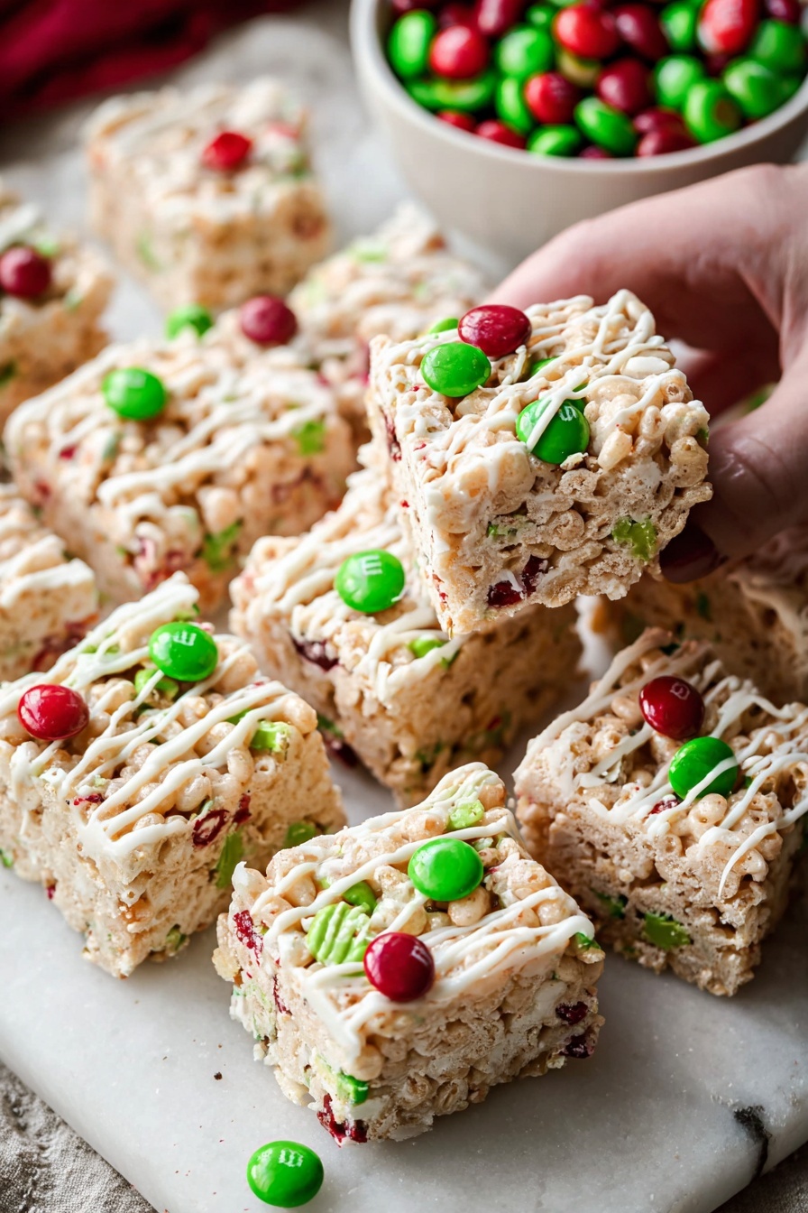 The image shows a close-up of two thick square treats, layered with light tan crispy cereal mixed with white marshmallow, topped with red and green candy-coated chocolates and red and green sprinkles. A white drizzle flows across the top of the treats in thin, uneven lines. The treats rest on brown parchment paper on a white marbled surface, with extra red and green candies scattered around. Below, a white bowl is filled with more red and green candy-coated chocolates, adding a festive touch. photo taken with an iphone --ar 2:3 --v 7