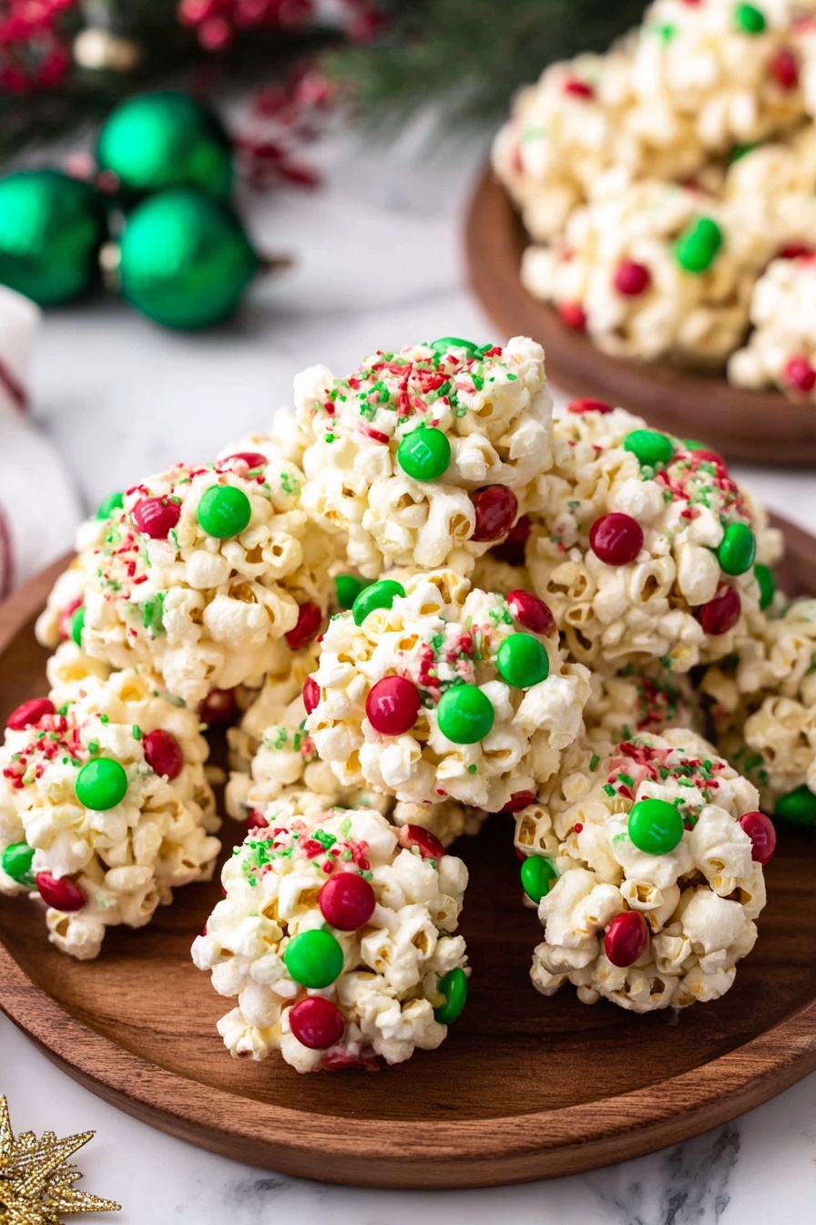 The image shows a wooden plate filled with round popcorn balls that have three layers of visible colors: the main layer is light cream popcorn, the second layer has small round candies in bright red and green, and the third layer includes tiny green and red sprinkles spread all over the popcorn balls. The popcorn balls are unevenly shaped but tightly packed, and the background has a white marbled texture with green ornaments and festive decorations in soft focus. photo taken with an iphone --ar 2:3 --v 7