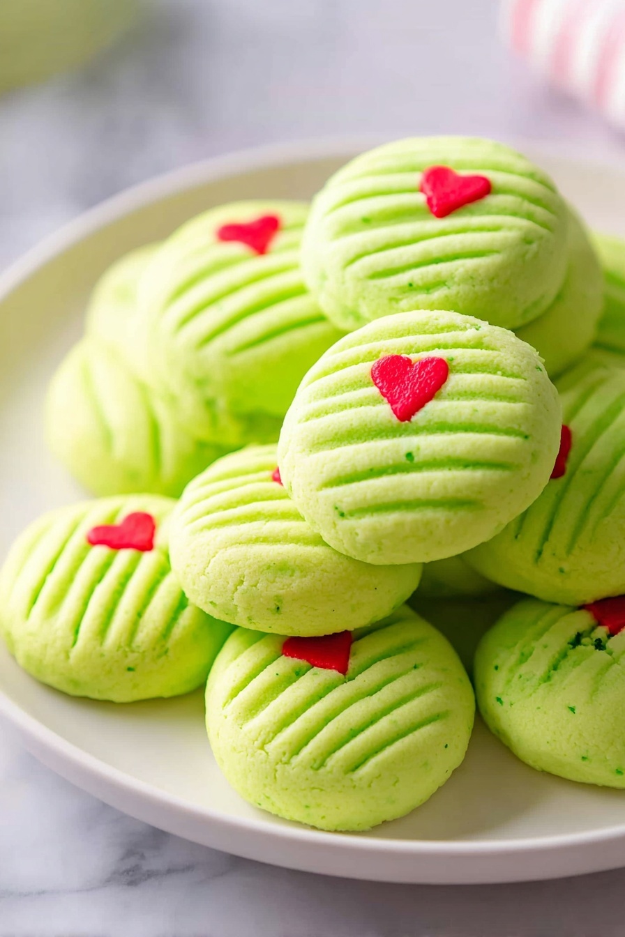 A pile of light green round cookies stacked on a white plate, each cookie has five parallel indent lines across the top giving a striped texture, and a small bright red heart-shaped decoration near the edge. The cookies have a smooth, matte finish and some show faint green specks. The plate sits on a white marbled surface, soft natural light brightens the scene, highlighting the gentle softness of the cookies. photo taken with an iphone --ar 2:3 --v 7