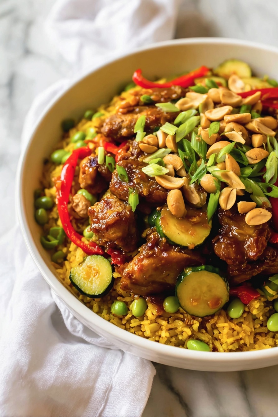 The image shows a white bowl filled with a colorful dish. The bottom layer has yellow rice mixed with small green peas and edamame beans, creating a textured base. On top of the rice, there are pieces of dark brown fried chicken coated in sauce. Scattered among the chicken pieces are sliced green zucchini and red bell pepper strips. Whole peanuts and small green chopped scallions are sprinkled over the dish, adding contrast in color and crunch. The bowl sits on a white marbled surface with a white cloth partially visible in the background. Photo taken with an iphone --ar 2:3 --v 7