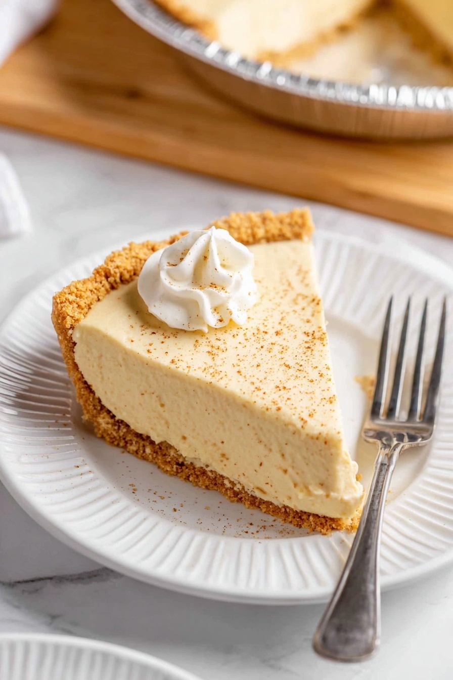 This image shows a creamy pie with two layers in a silver pie pan. The bottom layer is a thick, crumbly light brown crust that looks like crushed cookies. On top is a thick, smooth pale yellow filling with tiny dark specks inside. The top surface of the filling is sprinkled with a light dusting of brown powder. One slice has been removed, showing the clean, creamy texture of the filling and the crumbly crust underneath. The pie pan rests on a wooden board, and the scene has a white marbled texture background with a white plate partially visible. The photo taken with an iphone --ar 2:3 --v 7