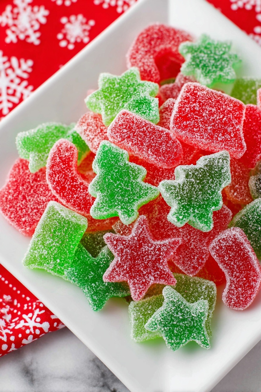 A white square plate filled with several layers of red and green gummy candies shaped like stars, Christmas trees, candy canes, bells, and stockings. Each candy is covered with a fine layer of sugar crystals that sparkle in the light. The candies overlap in a random pile, showing the different bright and clear colors with a slightly translucent look. The plate sits on a white marbled surface with a hint of a red cloth decorated with white snowflakes nearby. Photo taken with an iphone --ar 2:3 --v 7