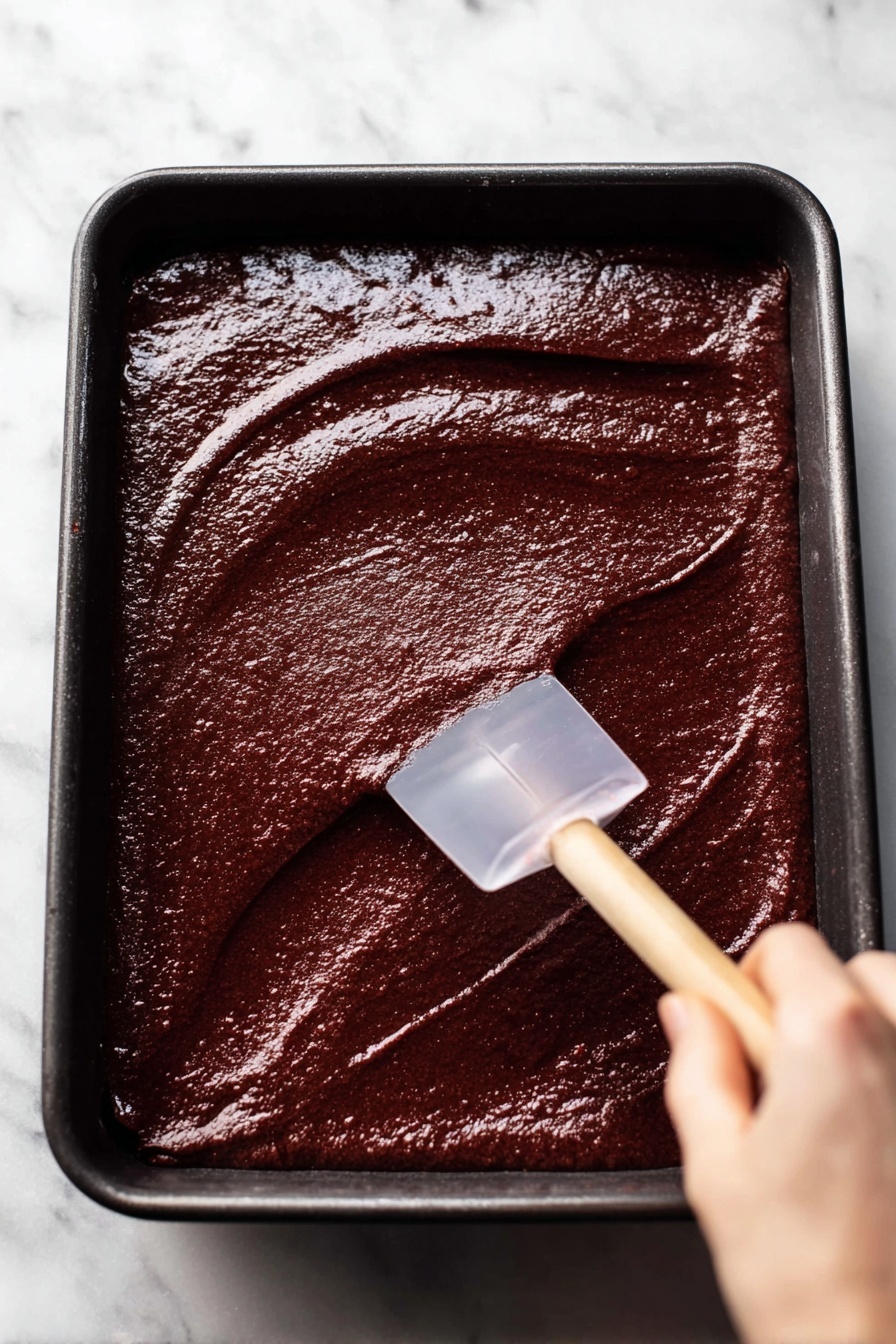 The image shows a close-up of slices of red velvet roll cake on white plates with a detailed silver rim. Each roll slice has two layers: a deep red, soft cake layer wrapped around a thick creamy white filling layered evenly in a spiral. The texture of the cake looks moist and fluffy, and the cream is smooth and thick. The plates rest on a white marbled surface. On one plate, there is a silver fork with the words
