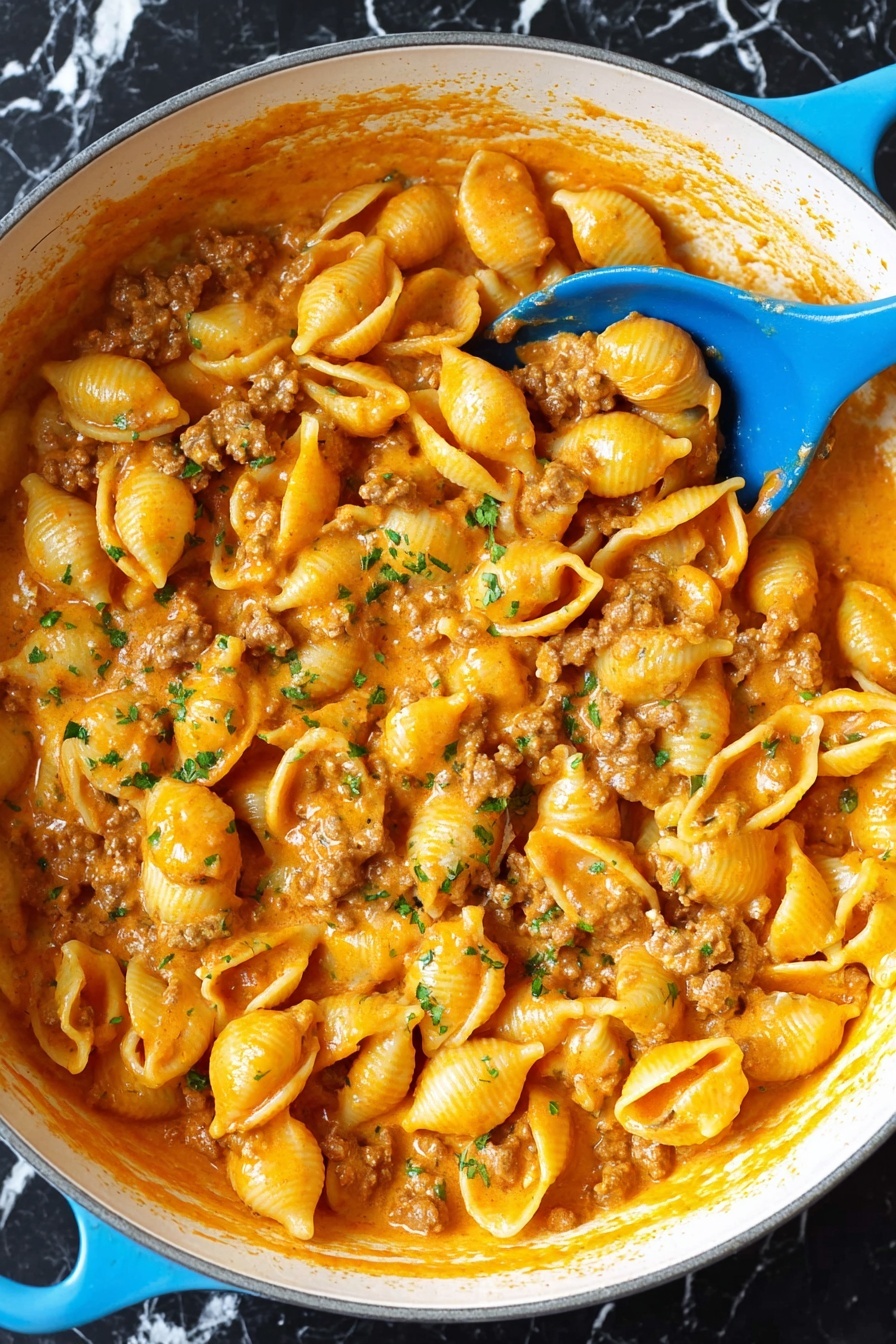 A large white pot filled with small shell pasta covered in creamy orange sauce mixed with browned ground meat pieces, garnished lightly with tiny green herb bits, with a bright blue spoon resting inside the pot; the sauce looks smooth and thick, coating every pasta shell evenly, and the pot is placed on a white marbled surface. photo taken with an iphone --ar 2:3 --v 7