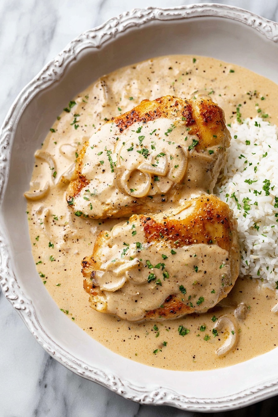 A silver frying pan with a metal handle sits on a black induction cooker placed on a white marbled surface. Inside the pan is a thick creamy sauce with slices of onion visible throughout, creating a swirled pattern. To the right, there is a white round plate with a bead-like edge detail holding five pieces of light brown cooked meat with slight golden sear marks. The overall look is clean and simple, focusing on the creamy onion sauce and the cooked meat against the white marbled surface. photo taken with an iphone --ar 2:3 --v 7