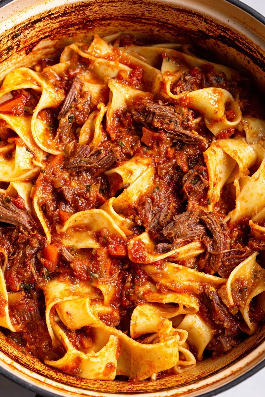 A close-up view of a pot filled with chunky pasta and slow-cooked meat sauce. The dish has wide, flat pasta noodles mixed with tender, shredded dark brown meat pieces, all coated in a thick, rich tomato sauce that has visible bits of carrots and herbs. The sauce is deep red with some darker, caramelized spots around the pot edges, showing the cooking process. The noodles have a light yellow color with a slightly soft texture, intertwined with the meat and sauce layers. The inside pot rim has a browned, rustic appearance, contrasting with the vibrant pasta and sauce inside. photo taken with an iphone --ar 2:3 --v 7