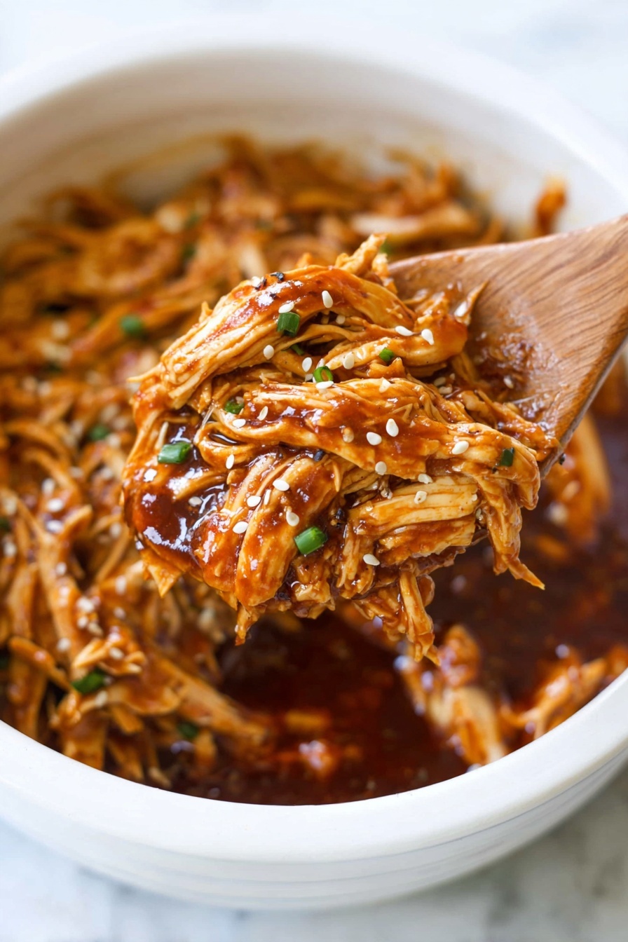 The image shows a close-up of shredded orange-brown cooked chicken mixed with a thick, glossy dark reddish-brown sauce inside a white bowl. The chicken strands look soft and juicy, with a few pieces sprinkled with small white and black sesame seeds and tiny green onion slices. A wooden spoon is lifting a portion of the sauced chicken, with the bowl filled with more shredded chicken and sauce visible in the background. The scene sits on a white marbled surface. photo taken with an iphone --ar 2:3 --v 7