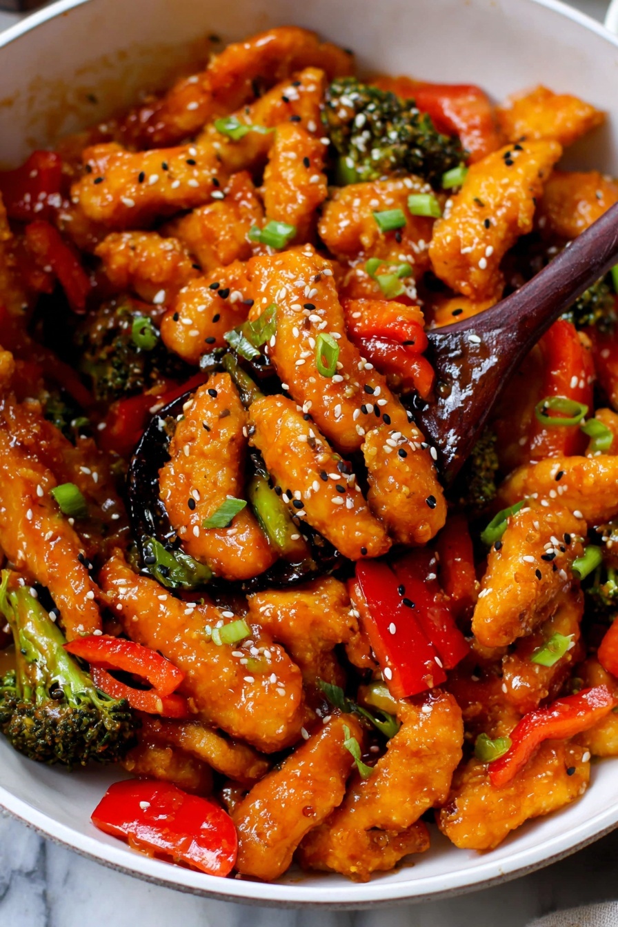 This image shows a close-up of a white bowl filled with vibrant orange chicken strips coated in a glossy sauce. Mixed in are bright red bell pepper slices and small green broccoli florets, adding color contrast. The dish is garnished with black and white sesame seeds and chopped green onions scattered across the top. A dark wooden spoon scoops up some of the chicken and vegetables from the center, lifting them slightly above the bowl. The background is a white marbled surface. photo taken with an iphone --ar 2:3 --v 7