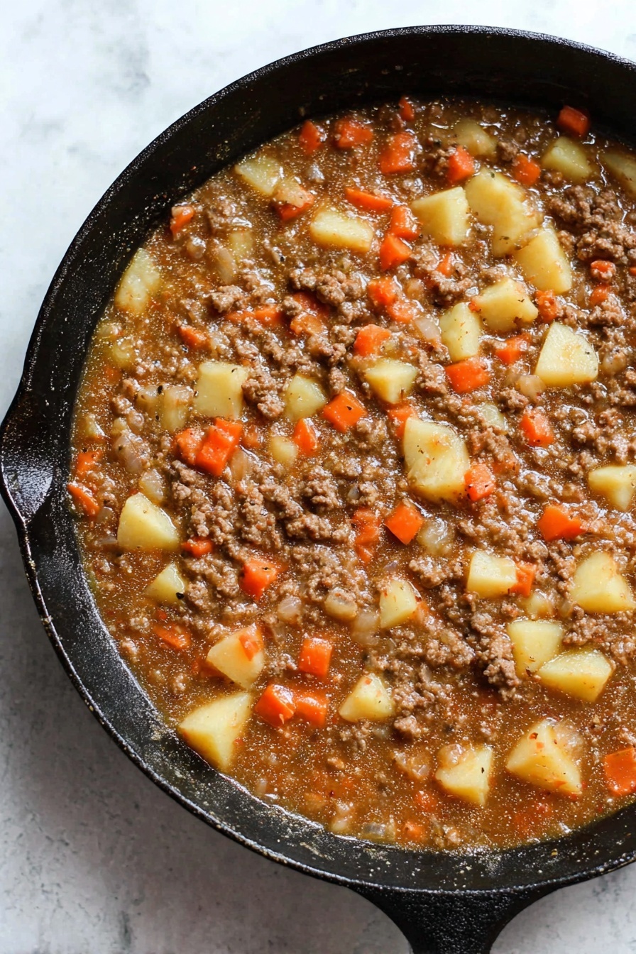 A close-up view of a black cast iron pan filled with a stew-like mixture, showing one main layer of a thick brown sauce with small chunks of cooked ground meat, medium-sized pale yellow potato cubes, orange carrot pieces, and small bits of translucent onion evenly spread throughout. The pan sits on a white marbled surface with visible texture and slight shadows around the edges. The colors are warm and earthy, with a mix of soft and slightly rough textures in the ingredients. photo taken with an iphone --ar 2:3 --v 7